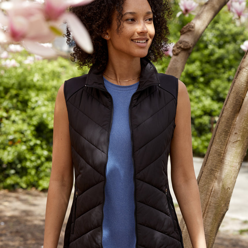 Woman wearing the Free Country Women's Quilted Hybrid Vest in black, featuring a unique quilted design with stretch knit panels and REPREVE® synthetic fill.