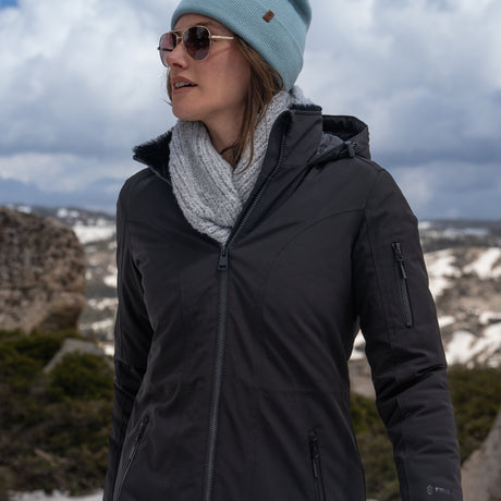 Woman wearing Free Country Women's Thermo Super Softshell® Long Jacket in black with a full front zipper opening, lower pockets, diamond quilted lining, a hood with an adjustable drawcord, and water resistant and wind resistant stretch performance fabric. Best women’s jacket for winter weather.