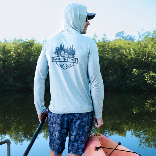 Man in light blue hoodie with nature-themed design by a body of water