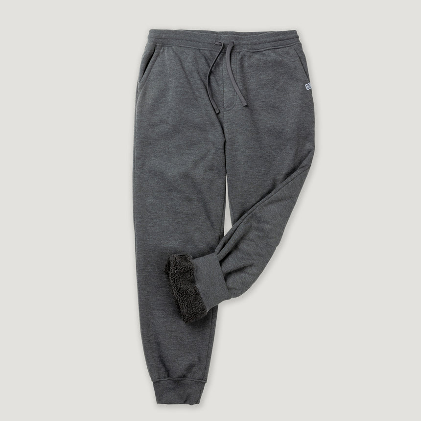 Man wearing Free Country Men's Sherpa Lined Jogger in dark grey with a drawcord waistband, soft lining, and side pockets, light grey background. Perfect men’s pants for fall weather.