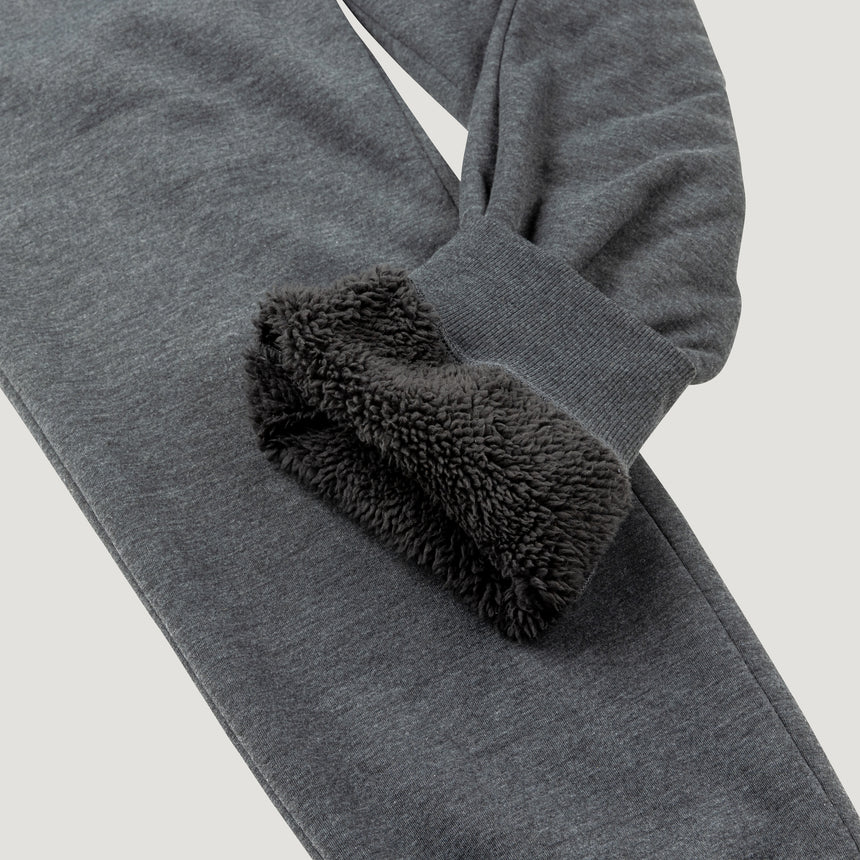 Man wearing Free Country Men's Sherpa Lined Jogger in dark grey with a drawcord waistband, soft lining, and side pockets, light grey background. Perfect men’s pants for fall weather.