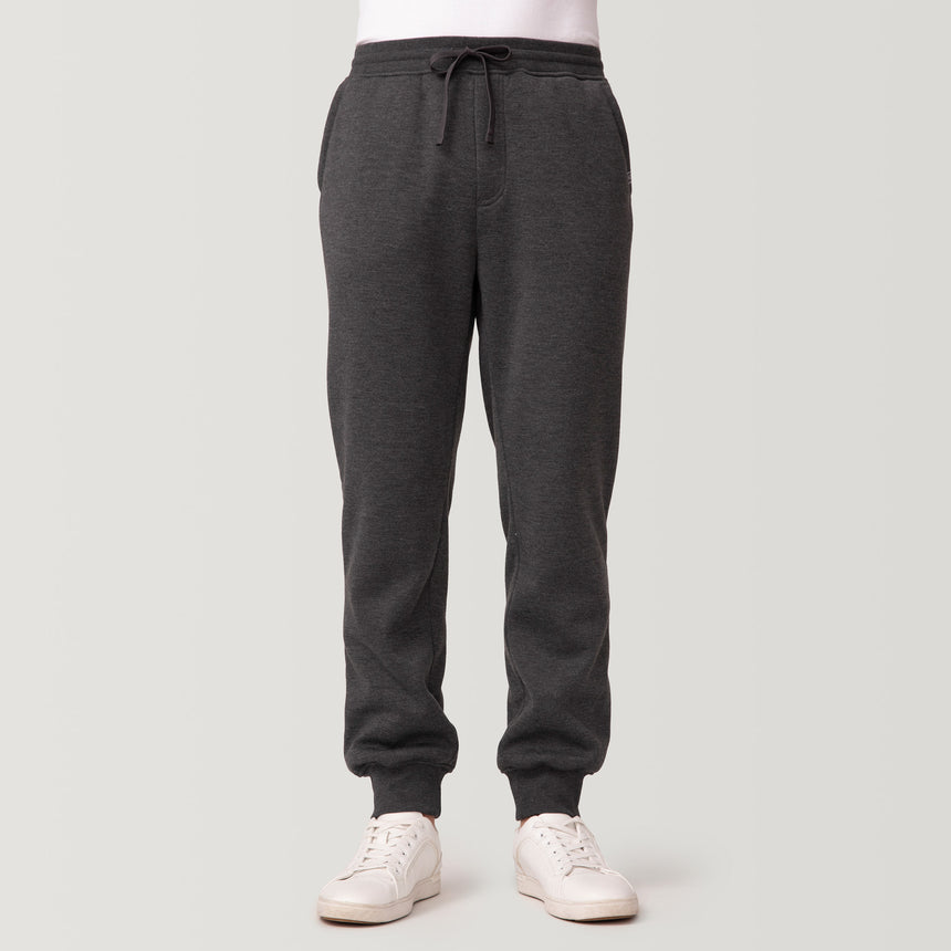 A person wears Free Country Men’s Sherpa Lined Jogger in Onyx Heather with white sneakers, standing against a light backdrop. Only the lower half is visible, highlighting stylish and comfortable athleisure wear.