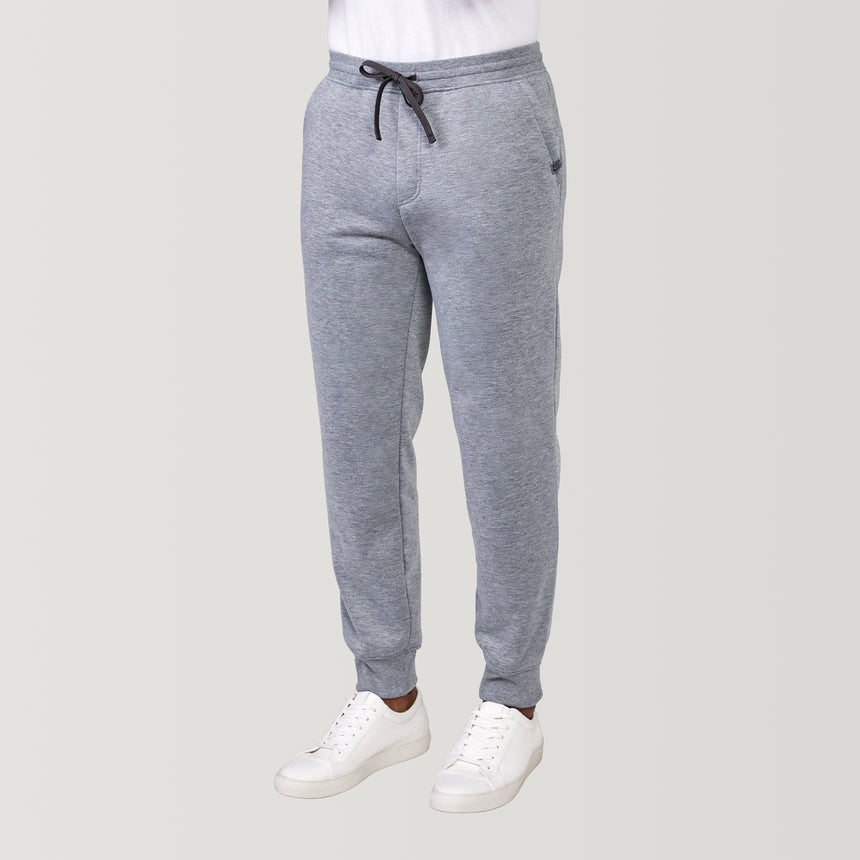 A person wearing Free Country Men’s Sherpa Lined Jogger in Grey Heather with a drawstring waist and white sneakers, standing against a plain light background.
