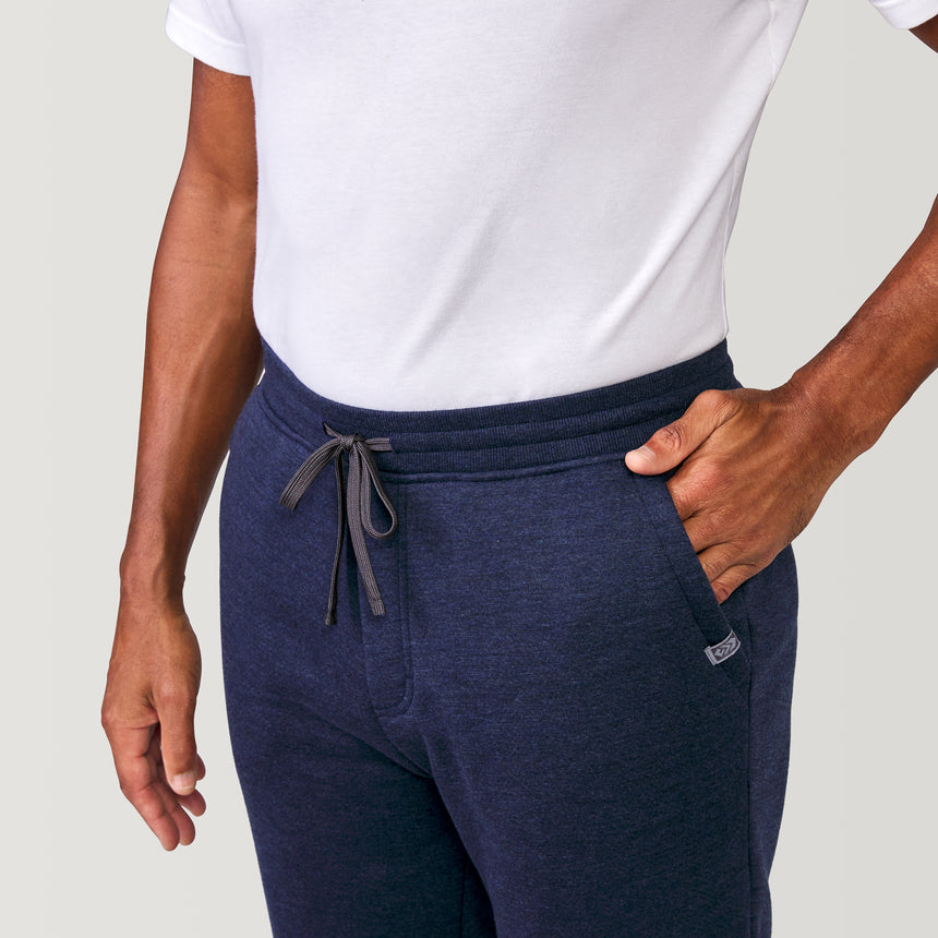 A man in a plain white t-shirt and Free Country Men’s Sherpa Lined Jogger stands with one hand in his pocket against a light gray background, showcasing casual athleisure style.