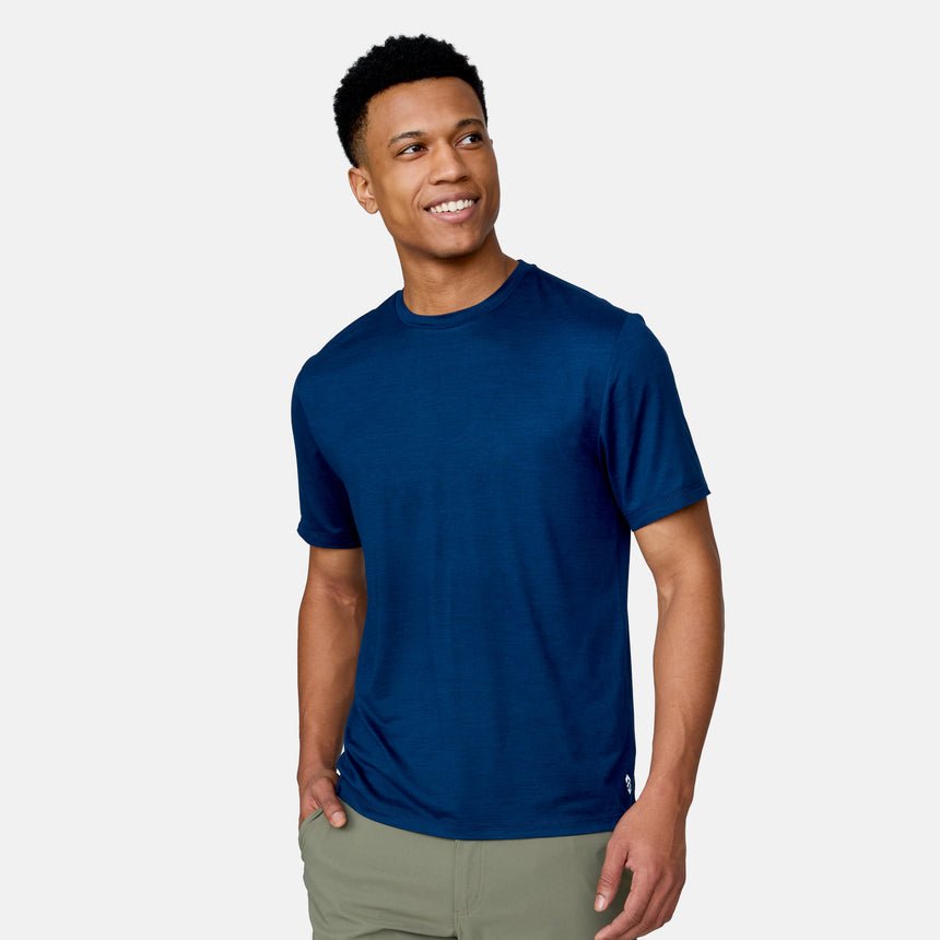 A man wearing the Clearance Men's Super Soft Short Sleeve Crew Tee from the 2 Pack in navy blue and light gray pants stands against a matching background, smiling and looking off to the side.