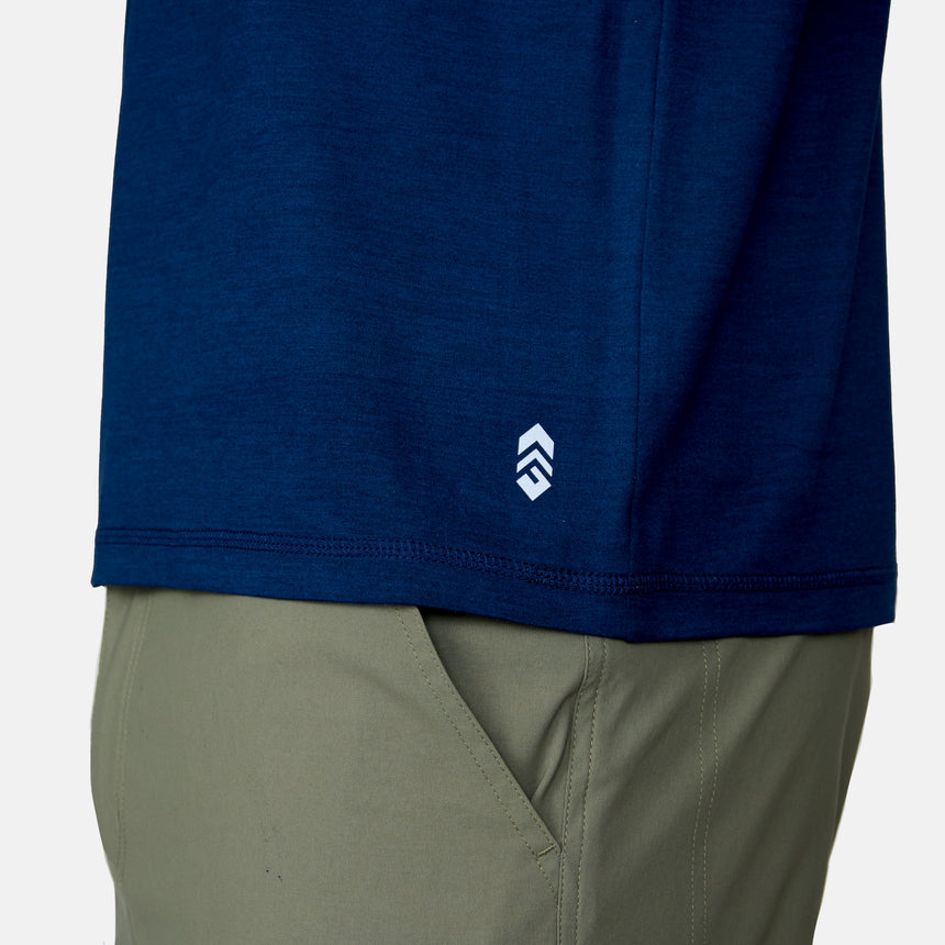 Close-up of a person wearing the Men's Super Soft Short Sleeve Crew Tee by Clearance in dark blue, featuring a small white logo near the hem, paired with light olive green pants and their hand in their pocket. This tee comes in a 2 pack.