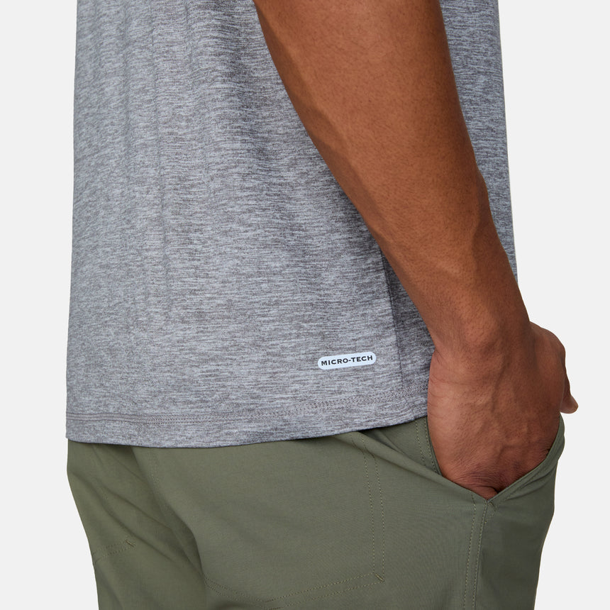 Close-up of a person wearing the Men's Super Soft Short Sleeve Crew Tee by Clearance in light gray heather, featuring a MICRO-TECH label and UPF 50+ sun protection. Paired with olive green pants, hand partly in pocket. White background. Sold as 2 pack.