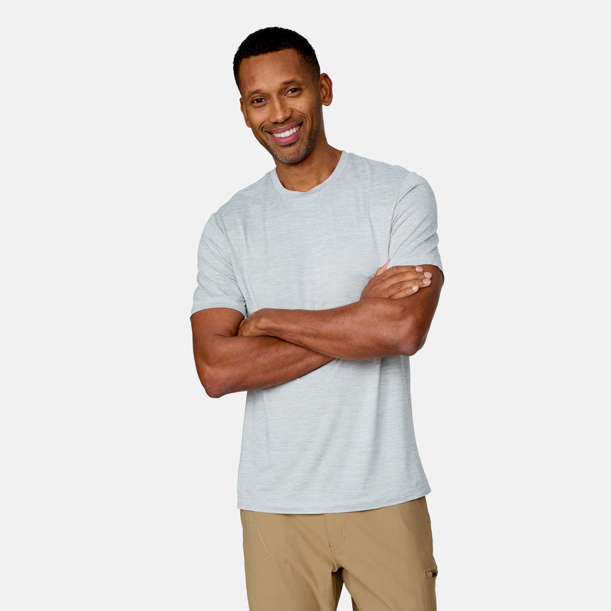 A man wears the Clearance Men's Super Soft Short Sleeve Crew Tee (2 Pack) in light gray with beige pants, standing against a white background, smiling with his arms crossed.