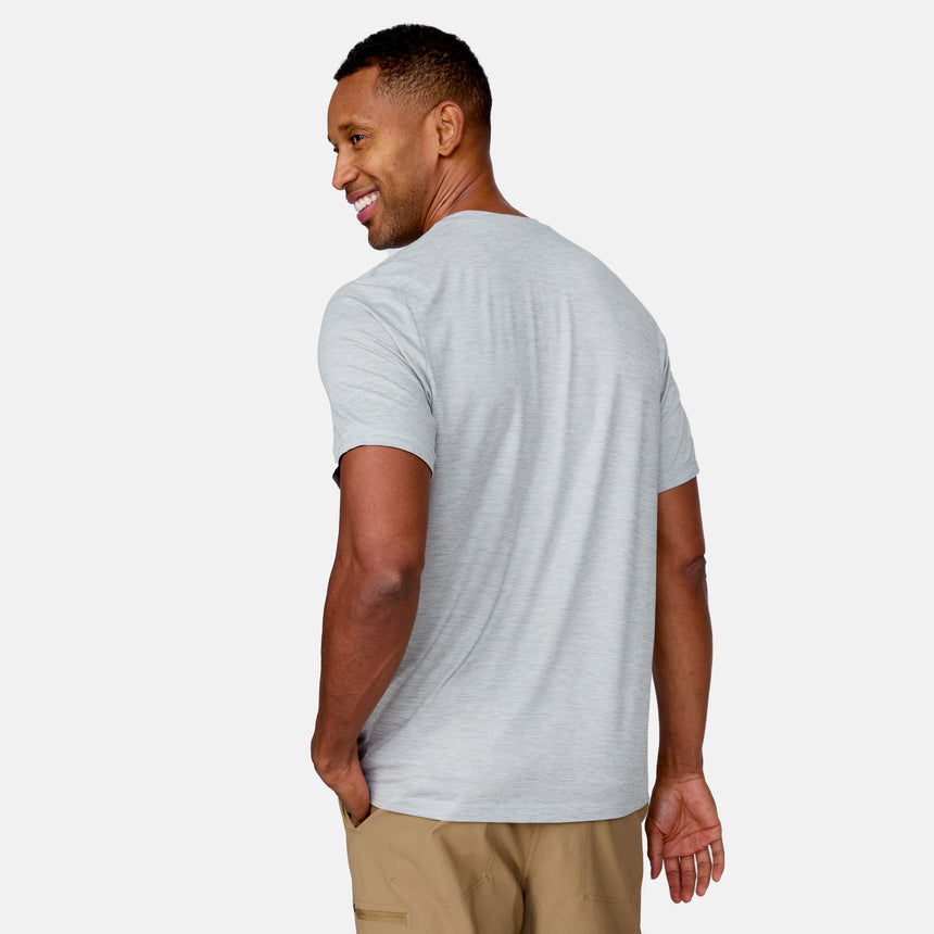 A man wears a light gray Men's Super Soft Short Sleeve Crew Tee from Clearance, part of a 2 Pack, with tan pants, standing against a plain white background and smiling over his shoulder.