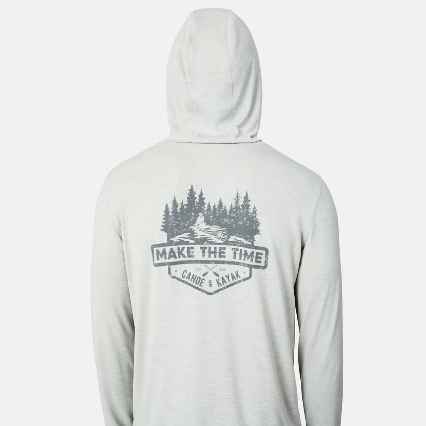 A person wears the Men's Microtech® Hooded Graphic Sunshirt by Free Country in light gray, featuring UPF 50+ protection and a back design with trees, a river, and "MAKE THE TIME CANOE & KAYAK" text.