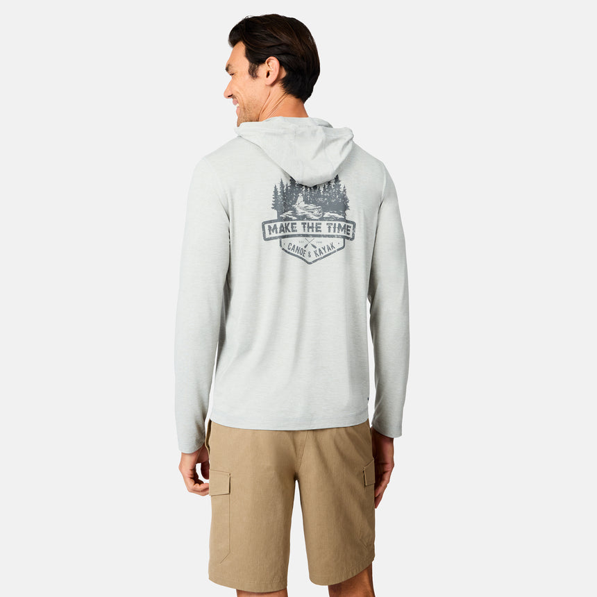 A man in a Free Country Men's Microtech® Hooded Graphic Sunshirt with moisture-wicking fabric and a "MAKE THE TIME" nature-themed back graphic, paired with tan cargo shorts, stands facing away on a white background.