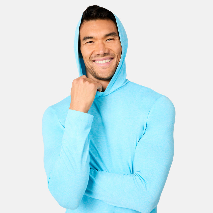 A smiling man in the Free Country Men's Microtech® Hooded Graphic Sunshirt with UPF 50+ stands against a white background, one arm crossed and the other holding his hood.