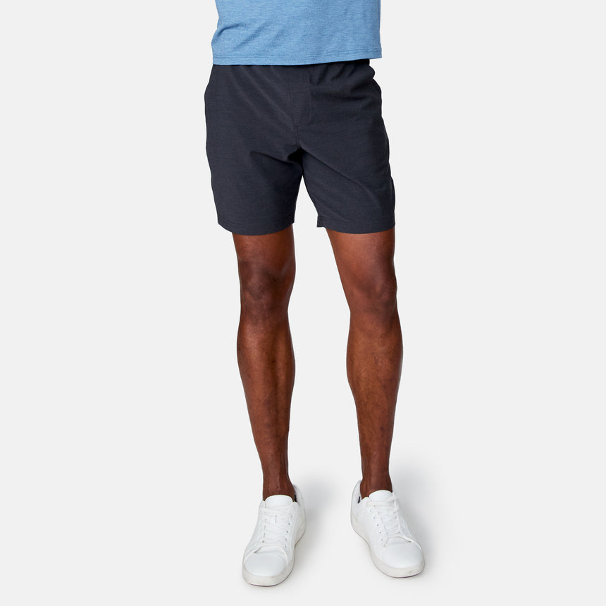 Wearing Clearance Men's Trek Short in dark blue, paired with white sneakers, a person stands against a plain light background. The image is cropped at the shoulders, showing only the lower body.