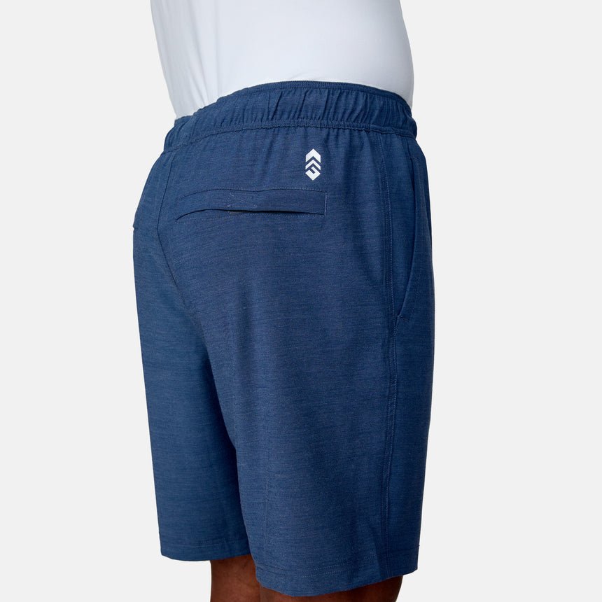 A man is seen from the back and side wearing Clearance Men's Trek Short in blue with an elastic waistband, back pocket, four-way stretch fabric, and a white logo above the pocket, paired with a white shirt.