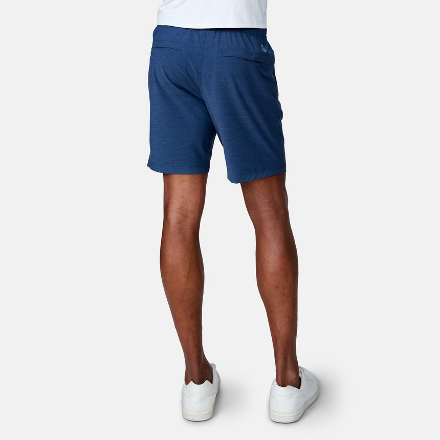 A person is shown from the back, standing against a light gray background, wearing a white shirt, white sneakers, and Clearance Men's Trek Short in blue with four-way stretch.