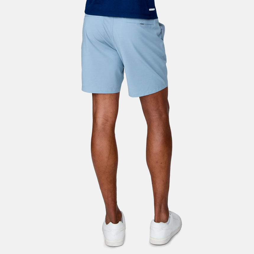A person stands facing away from the camera against a plain white background, wearing Clearance Men's Trek Short in light blue, a dark blue shirt, and white sneakers.