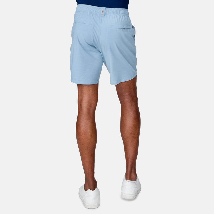 A person in Clearance Men's Trek Short in light blue, a blue shirt, and white sneakers stands facing away from the camera against a plain white background.