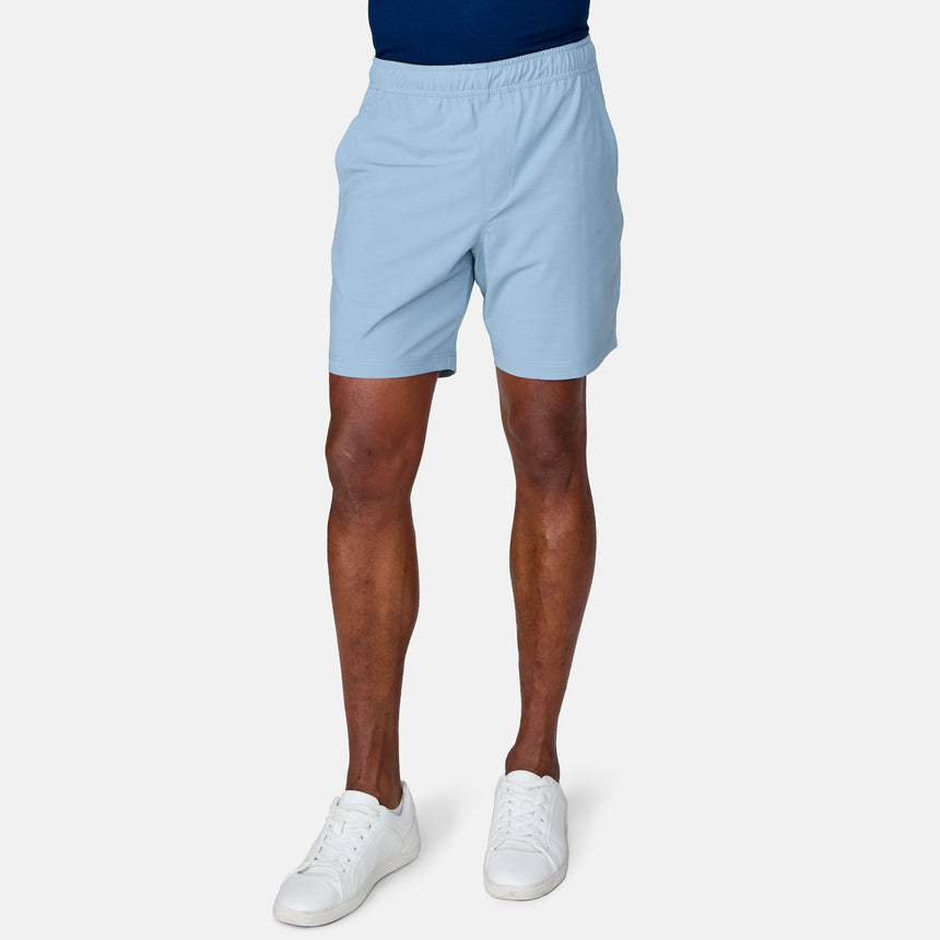 A person stands against a plain white background, showing only their lower body while wearing Clearance Men's Trek Shorts in light blue, paired with a navy shirt and white sneakers.