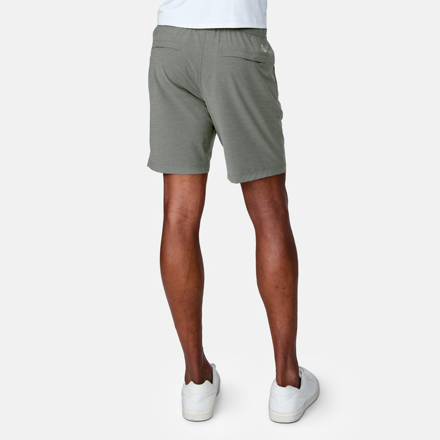 Only the lower half of a person is visible as they stand facing away from the camera, wearing Clearance Men's Trek Short in light green and white sneakers against a plain, light background.
