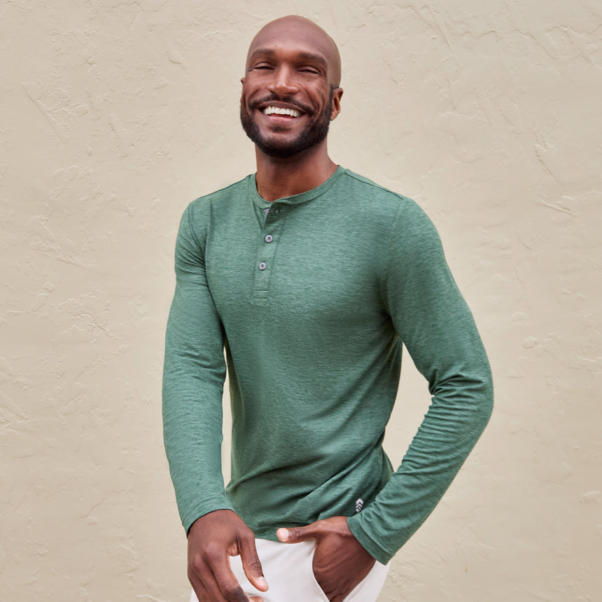 Man wearing Free Country Men's Henley Long Sleeve Shirt in Cilantro, size M, made from lightweight soft polyester fabric featuring a classic fit with anti odor and upf technology, styled with white shorts #color_cilantro