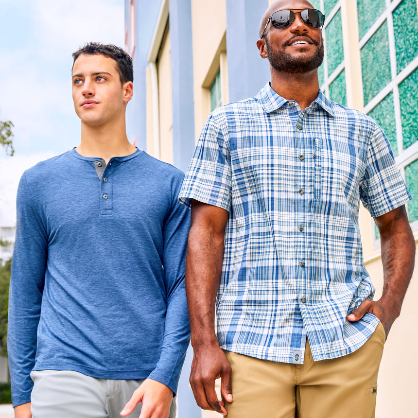 Man wearing Free Country Men's Henley Long Sleeve Shirt in Steel Blue, size M, made from lightweight soft polyester fabric featuring a classic fit with anti odor and upf technology, styled with grey shorts #color_steel-blue