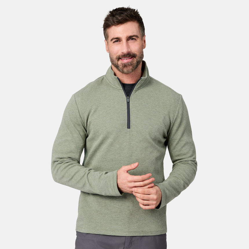 A man with short dark hair and a beard is standing and smiling against a plain white background, wearing the Free Country Men’s Twill Interlock 1/4 Zip Long Sleeve Shirt in Moss Heather and gray pants.