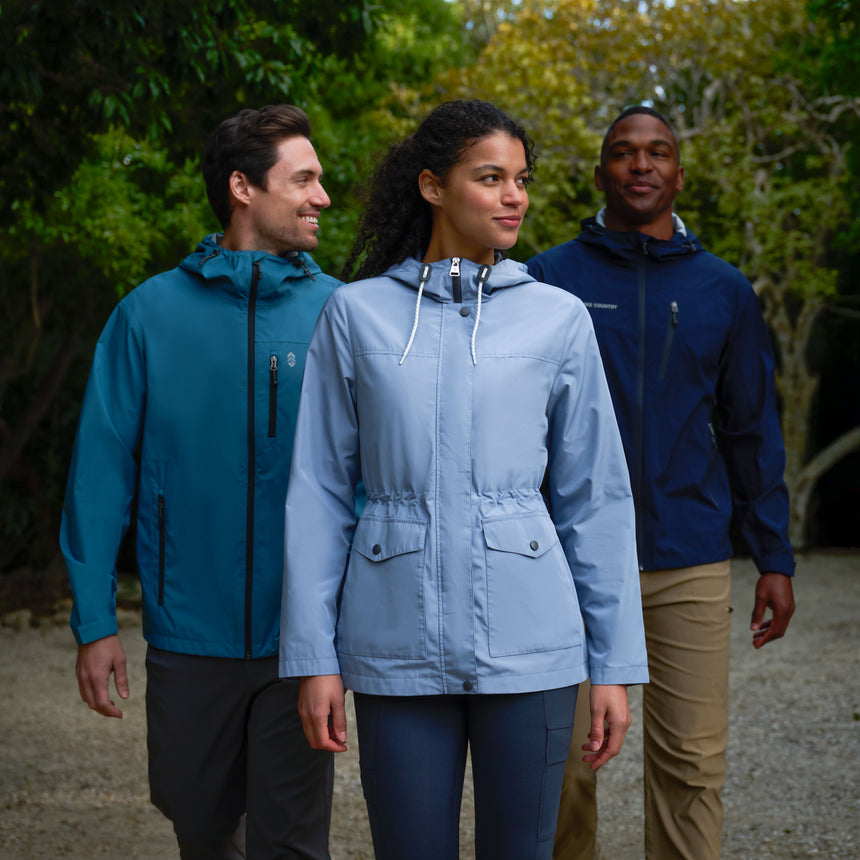 Three people wearing raincoats walking outdoors with trees in the background