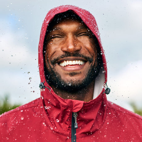 Man wearing Free Country Men's Hydro Lite X2O Highline Waterproof Jacket in Redrock, size M, made from lightweight performance polyester fabric featuring a sealed seams and an attached hoop with a drawcord and cord lock, styled with blue jeans #color_redrock