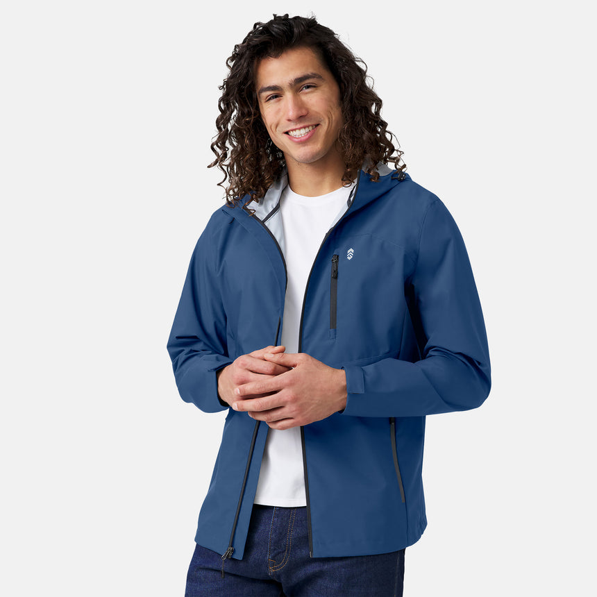 A man with long curly hair smiles while wearing the Clearance Men's Hydro Lite X2O Highline Waterproof Jacket over a white t-shirt and blue jeans, standing against a plain light background.