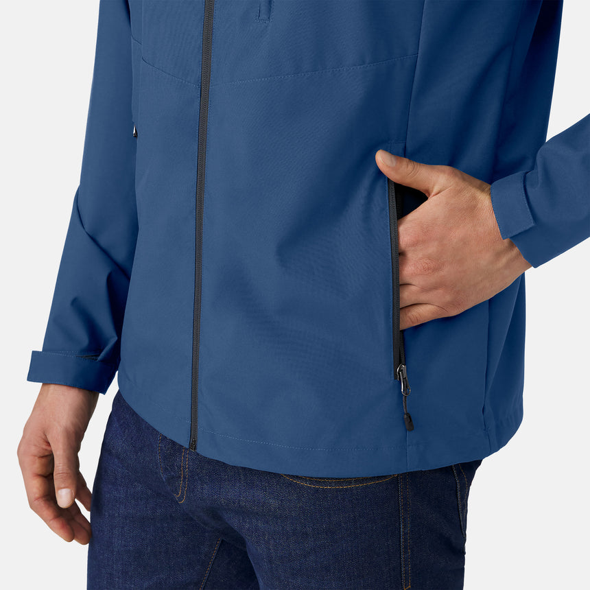 A person wearing the Clearance Men's Hydro Lite X2O Highline Waterproof Jacket in blue and dark jeans unzips the jacket’s side pocket with their right hand. The background is plain and light-colored.