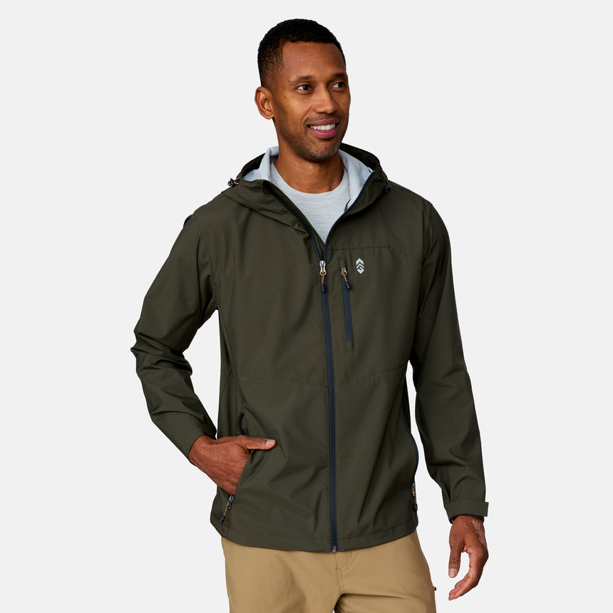 A man wearing the Clearance Men's Hydro Lite X2O Highline Waterproof Jacket in dark green over a light gray shirt and khaki pants stands smiling with one hand in his pocket against a plain, light background.