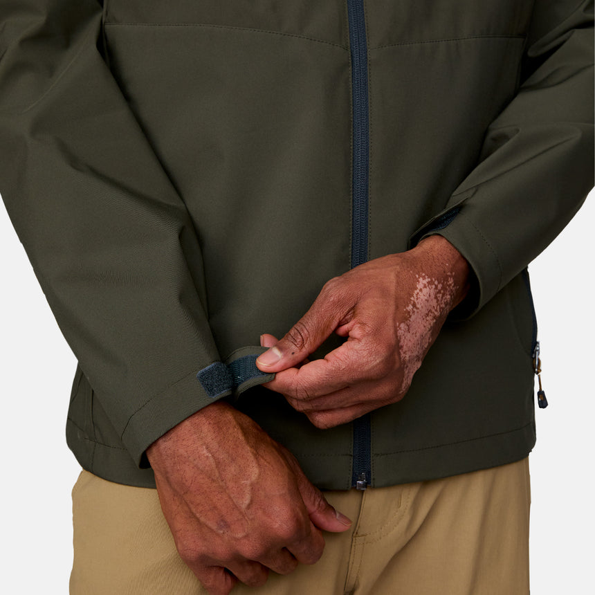 A person with vitiligo on their hand fastens the cuff of a Men's Hydro Lite X2O Highline Waterproof Jacket by Clearance, in olive green, using a hook-and-loop strap. They wear tan pants.