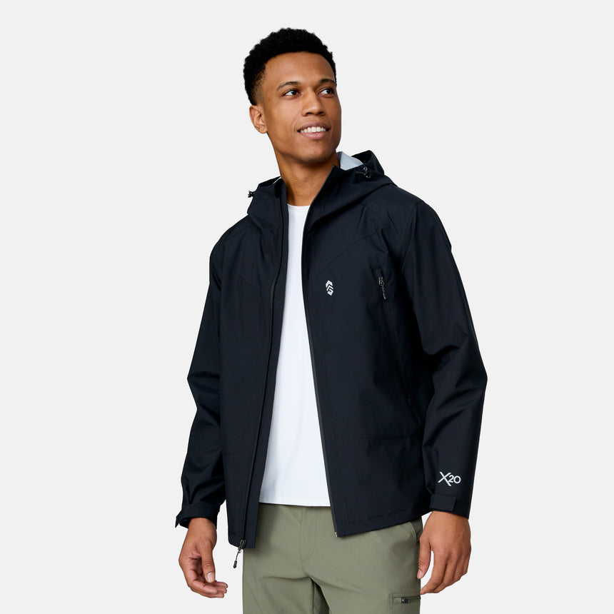 A man wears the Clearance Men's Hydro Lite X2O Squall Rain Jacket in black over a white shirt and olive green pants, standing against a plain light background while looking to the side and smiling.