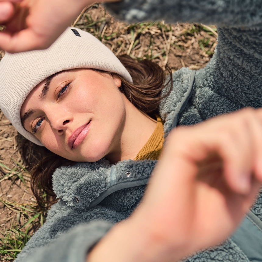 Person wearing a gray fleece jacket and white beanie lying on the ground.