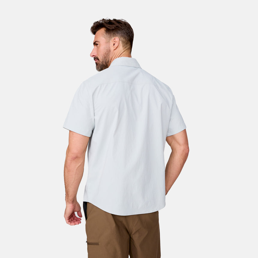 A man with short brown hair and a beard wears the Clearance Men's Explorer Short Sleeve Shirt in light gray and brown pants, facing away and slightly to the side against a plain white background.