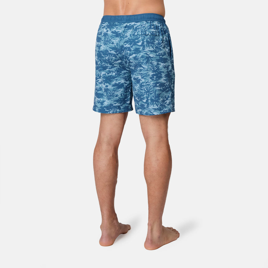 A person stands barefoot on a white background, seen from behind wearing Free Country's Men's Surf Camo Swim Short, showcasing the blue camo pattern and UPF 50+ protection.
