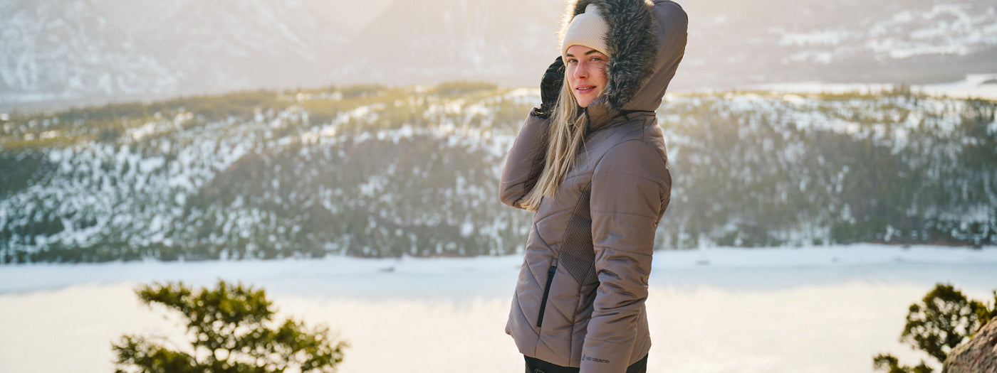 Woman in a winter coat standing in a snowy landscape with mountains in the background