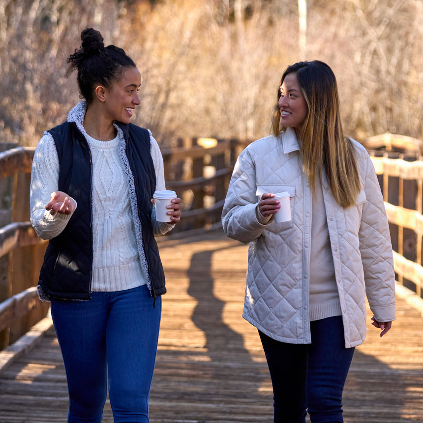 Woman wearing Free Country Women's Expedition Stratus Lite Reversible Vest in black with a full front zipper opening, soft lining, recycled polyester filling, and water resistant and wind resistant performance fabric. Best women’s vest for chilly weather.