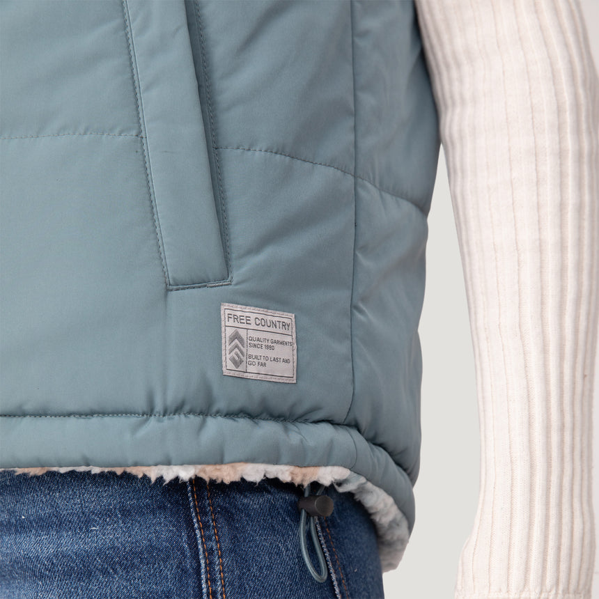 Woman wearing the Free Country Women's Venture Stratus Lite Reversible Vest in light blue, featuring a geometric-print Butter Pile® lining and horizontal quilted overlay