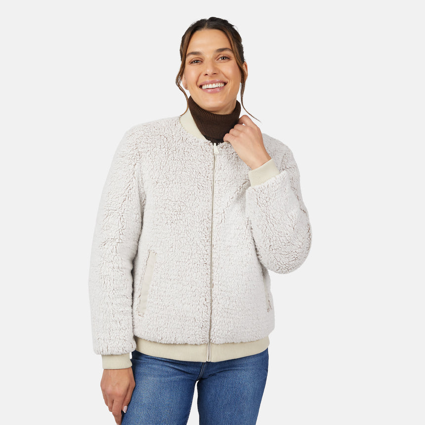 A woman smiles while wearing the Clearance Women's Stratus Lite Reversible Quilted Bomber Jacket over a dark turtleneck and blue jeans, standing against a plain white background.