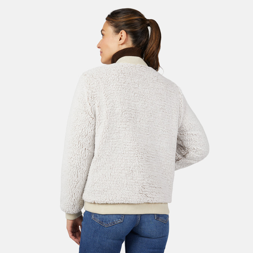 A woman with brown hair in a ponytail faces away, wearing the Women's Stratus Lite Reversible Quilted Bomber Jacket by Clearance and blue jeans, set against a plain white background.