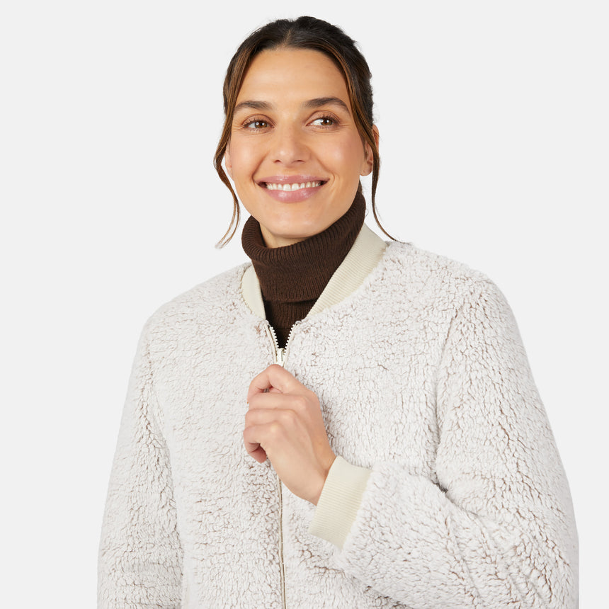 A woman smiles in the Clearance Women's Stratus Lite Reversible Quilted Bomber Jacket, cream-colored with quilted details, layered over a brown turtleneck and posed against a plain white background.