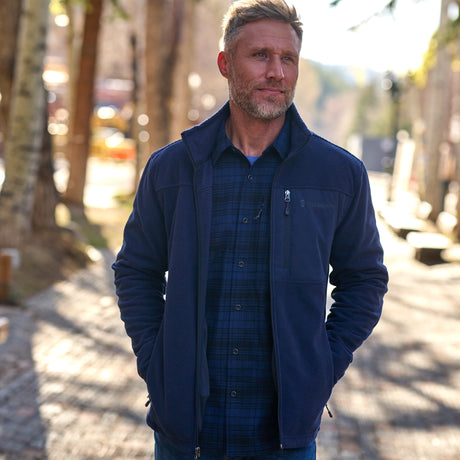 A man wearing a black fleece jacket with a full zip front closure, standing with hands in pockets.