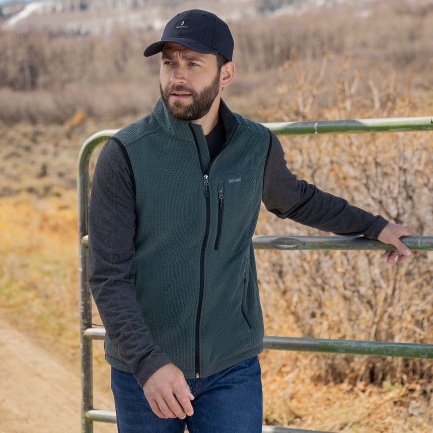 Man wearing a green Free Country vest and black cap standing in a field