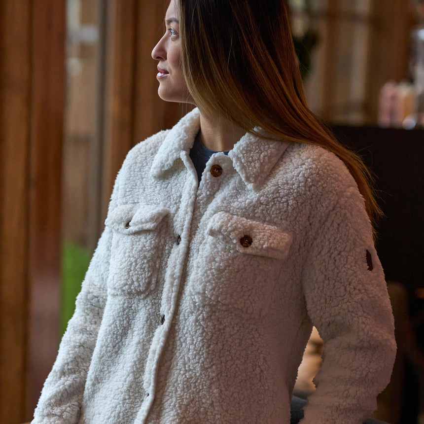 Woman wearing Free Country Women's Sherpa Shacket in white with a full front button opening, stand collar, chest pockets, and soft sherpa fabric. light grey background. Perfect women’s jacket for fall weather.