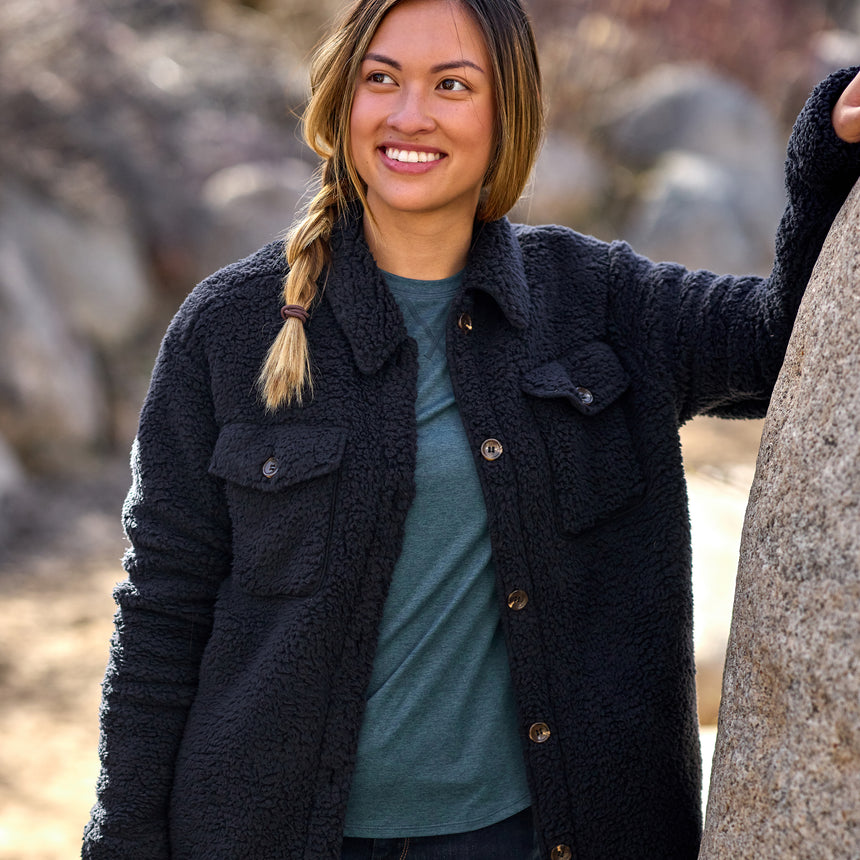 Woman wearing Free Country Women's Sherpa Shacket in black with a full front button opening, stand collar, chest pockets, and soft sherpa fabric. light grey background. Perfect women’s jacket for fall weather.