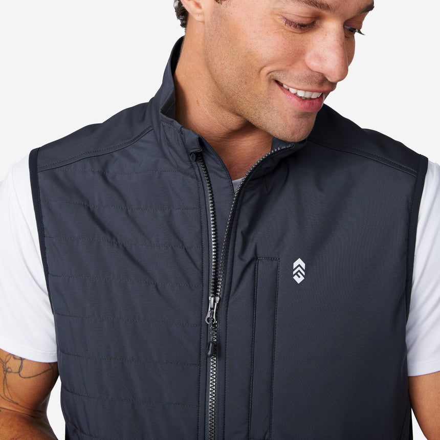 A man wearing the Clearance Men's High Stretch Full Zip Vest in dark gray over a white short-sleeve shirt smiles and looks down. The vest features a small chest logo, vertical zipper pocket, and water-resistant fabric.