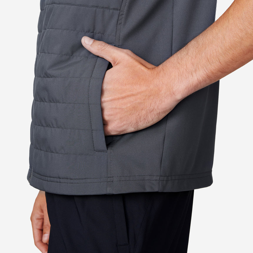 A person wears the Clearance Men's High Stretch Full Zip Vest in gray, featuring recycled polyfill, and dark pants. Their right hand is in a side pocket against a plain, light background.