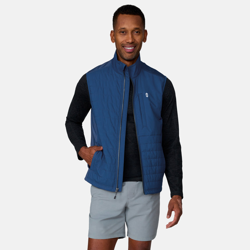 A man smiles while wearing the Clearance Men's High Stretch Full Zip Vest over a black long-sleeve shirt and light gray shorts. One hand is in his vest pocket, against a plain, light-colored background.