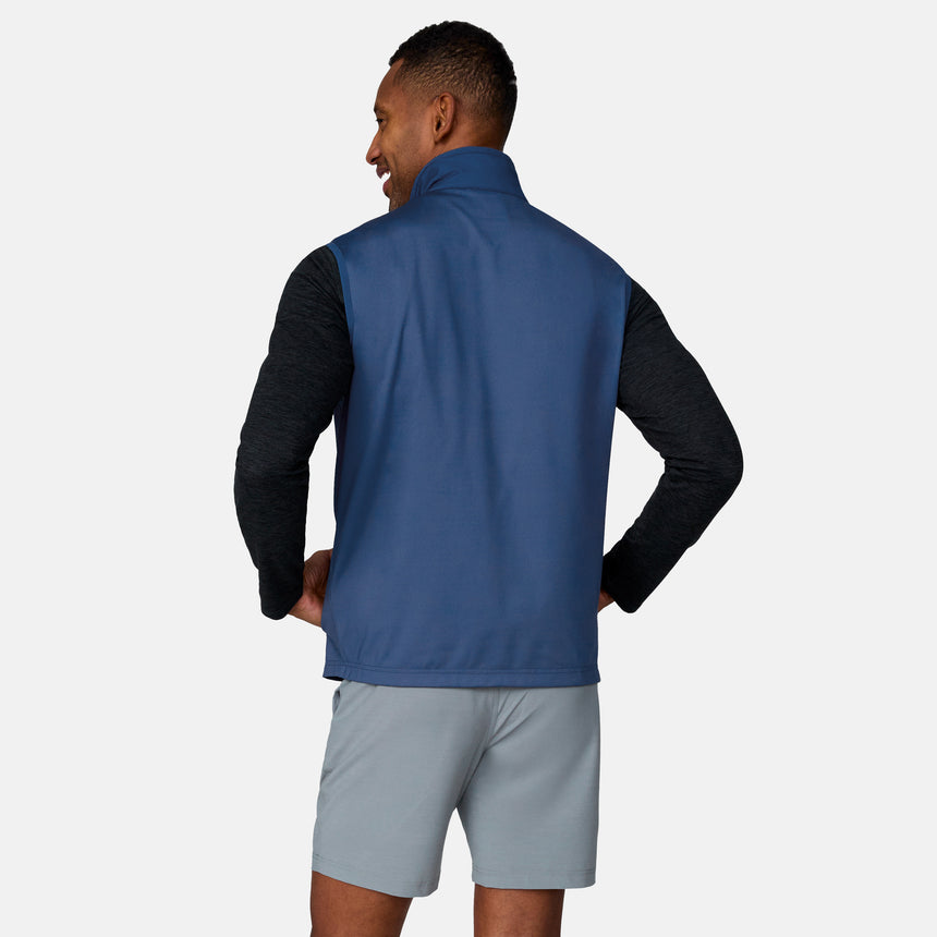 A man stands with his back to the camera, modeling the Clearance Men's High Stretch Full Zip Vest over a black long-sleeve shirt and light gray shorts, hands on hips against a plain light background.